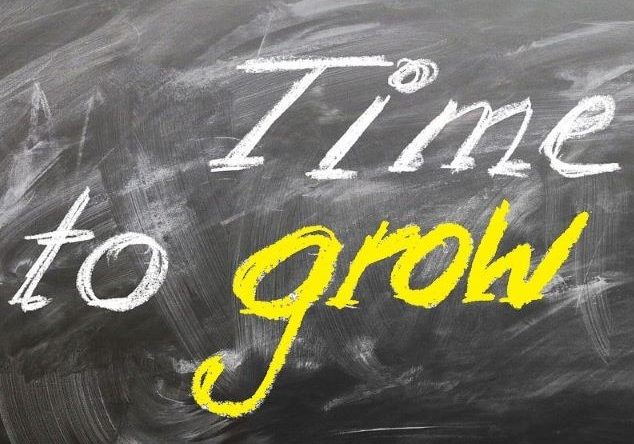 Hand hält ein Tablet, umgeben von Begriffen zu Lernen, Kompetenz und Wachstum auf schwarzem Hintergrund.