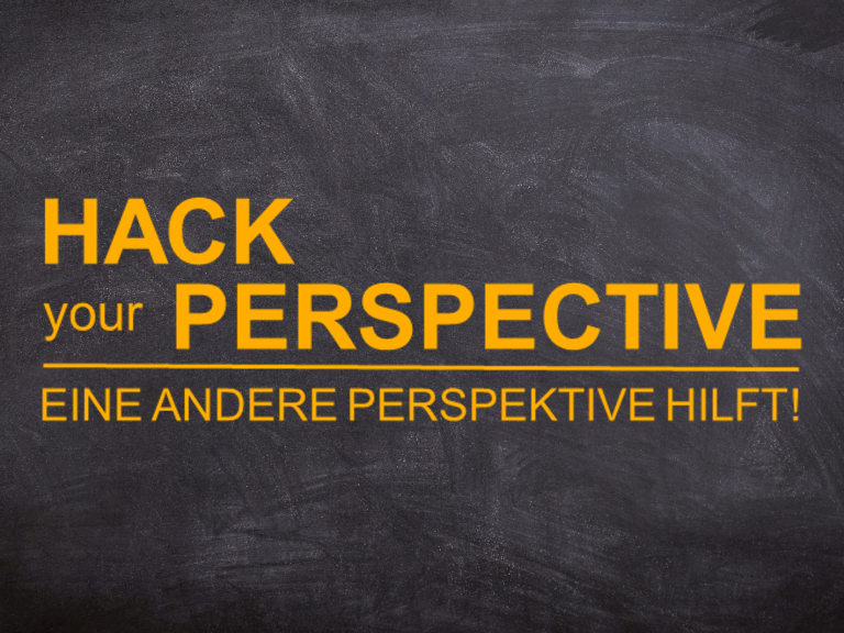 Schwarze Tafel mit dem Text "Hack your Perspective" in orange und der deutschen Übersetzung.