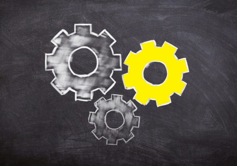 Prozesse Drei Zahnräder auf einer Tafel, zwei in Grau und eines in Gelb.