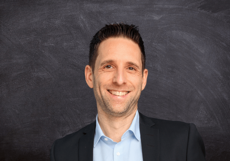 Management Mann in Anzug mit freundlichem Lächeln vor dunklem Hintergrund.